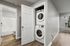 Modern apartment with in-unit stacked washer and dryer next to a sleek bathroom, featuring stylish wood flooring and abundant natural light through large windows.