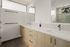 Luxurious modern bathroom with dual sinks, elegant light wood cabinetry, and stylish tile accents. Bright and spacious with chic minimalist design.