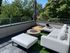 Elegant rooftop patio featuring a modern outdoor lounge set with lush greenery views and a cozy fire pit.