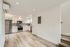 Modern kitchen with stainless steel appliances, white cabinetry, and sleek gray backsplash in an open-concept living space.