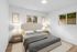 Cozy modern bedroom with elegant decor, featuring a plush bed, stylish lamps, and natural light from two windows.