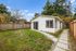 Charming modern backyard studio with fresh landscaping, bordered by a wooden fence and surrounded by lush trees.