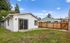 Charming backyard view of a quaint white house with a sliding glass door, vibrant green lawn, and privacy wood fence under a bright blue sky.