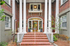 Elegant entrance with classic columns and brick facade leading to a welcoming doorway, surrounded by lush greenery.