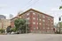 Charming brick apartment building situated on a street corner with lush greenery and urban skyline views.