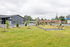 Charming residential area with modern building facade, lush green lawn, and community seating, offering a welcoming suburban atmosphere.