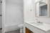 Bright modern bathroom featuring a sleek vanity unit, elegant mirror, and pristine bathtub with shower.