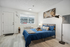 Bright, modern bedroom featuring a cozy bed with blue linens, elegant wall art, and natural light from a large window.