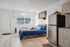 Contemporary studio apartment featuring cozy sleeping area, modern kitchen with stainless steel fridge, and natural light through large window.