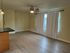 Spacious and bright living room with elegant wood flooring, modern ceiling fan, and ample natural light through large windows with chic curtains.
