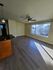 Bright and modern apartment interior showcasing stylish wood flooring, a ceiling fan, and a large window with serene views, ideal for urban living.