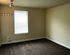 Bright and cozy room featuring warm neutral walls, plush carpeting, and a large window with blinds, offering ample natural light.