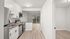 Modern kitchen with stainless steel appliances, sleek cabinetry, and light wood flooring leading to a bright living room with large windows.