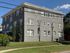 Charming three-story brick apartment building with large windows and manicured greenery, set against a clear blue sky.