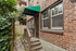 Charming brick exterior with green awning and quaint entryway, surrounded by lush greenery.