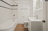 Elegant white bathroom featuring a classic bathtub, sleek wooden flooring, and modern vanity.