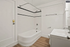Elegant modern bathroom with sleek white tiles, a luxurious bathtub, and stylish wood flooring.