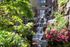Lush garden with a cascading waterfall surrounded by vibrant pink flowers and green foliage, creating a serene and enchanting outdoor space.