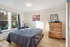 Bright and cozy bedroom with large windows, chic decor, and a stylish wooden dresser.