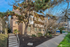 Charming apartment building with tree-lined walkways and modern architectural design under a bright blue sky.