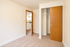 Bright bedroom with plush carpet, open closet space, and warm wooden accents leading to a modern kitchen.