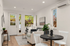Bright and inviting living room with modern decor, featuring a cozy couch, elegant table with white chairs, and lush greenery visible through large windows.