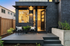 Charming modern apartment entrance with stylish black brick facade, cozy outdoor seating, and welcoming warm interior lighting.