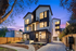 Modern three-story townhouse with large windows and elegant exterior lighting, nestled in a serene neighborhood at twilight.
