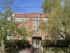 Charming brick apartment building with large windows surrounded by lush greenery, featuring a welcoming entrance and vibrant urban atmosphere.