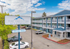 Charming exterior of The Theodore Apartments featuring modern design, lush greenery, and ample parking under a vibrant blue sky.