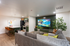 Inviting open-plan living room with plush gray sofa, vibrant green accents, and stylish modern kitchen featuring a breakfast bar and elegant lighting.