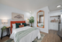 Cozy bedroom with modern decor featuring a vibrant orange headboard, soft bedding, elegant mirrors, and a chic mini kitchen area.