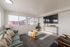 Bright and modern living room with large windows, cozy furnishings, and a stylish glass coffee table.