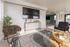 Bright and modern living room with chic decor, featuring a large flat-screen TV, stylish seating, and a glass coffee table, creating a welcoming and elegant atmosphere.