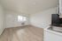 Bright studio apartment featuring modern wood flooring, ample natural light through a large window, and a compact kitchen area.