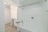 Bright, contemporary bathroom featuring a gleaming white bathtub and modern fixtures, leading into a space with sleek cabinetry and ambient lighting.
