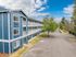 Modern blue apartment building with white balconies, surrounded by greenery, ample parking space, and a clear blue sky backdrop.