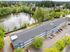 Aerial view of a modern apartment complex surrounded by lush greenery next to a serene lake, offering a tranquil living environment.