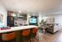 Modern open-concept living space featuring a chic kitchen with green cabinets, stylish bar seating, and a cozy living area with a large TV and elegant decor.