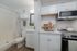 Chic compact kitchen and bathroom space with modern white cabinetry, stainless steel appliances, and elegant decor touches.