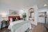 Inviting bedroom with a vibrant orange headboard, plush pillows, stylish greenery, and a large decorative mirror beside a cozy kitchenette.