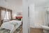 Inviting bedroom with natural light, chic decor, and warm wooden flooring adjacent to a modern bathroom.