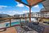 Charming outdoor patio overlooking a sparkling pool with stylish seating, framed by modern apartment buildings under a clear blue sky.