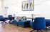 Modern lounge area featuring stylish blue chairs, a patchwork bench, and a chic abstract artwork, perfect for relaxation and socializing.