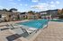 Luxurious outdoor swimming pool area featuring stylish lounge chairs, surrounded by modern architecture under a clear blue sky.