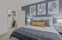Chic bedroom featuring a plush bed with patterned cushions, stylish wall art, and a neatly organized walk-in closet, complemented by soothing blue accent wall.