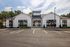 Charming modern apartment exterior with sleek white paneling and large windows, surrounded by lush greenery and ample parking space.
