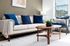 Modern living room with a stylish beige sofa, accented by plush blue pillows and a cozy knit throw. Elegant wooden coffee table and chic decor enhance the inviting ambiance.
