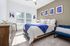Sunlit bedroom featuring a cozy bed with a blue throw, stylish art on the walls, and modern furnishings for a serene ambiance.