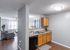 Modern apartment kitchen with sleek cabinetry, open access to a bright living area featuring cozy seating and large windows.